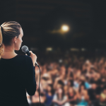 Back of Woman Giving Speech in Front of a Crowd