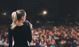 Back of Woman Giving Speech in Front of a Crowd