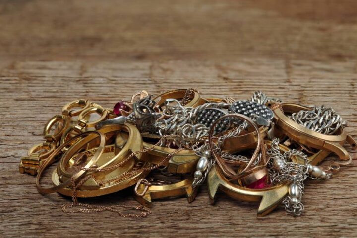 A small pile of tangled gold and silver necklaces and rings on a wooden surface.