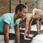 A woman does pushups on a mat in an exercise class. Alongside her are other members of the class in pushup positions.